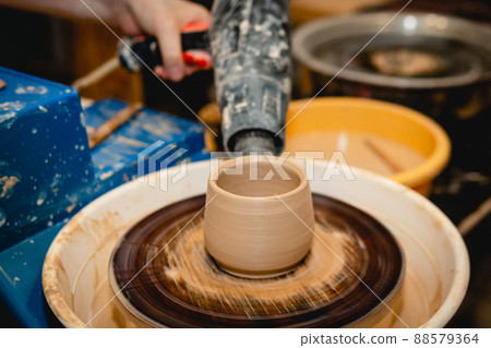 Potter working on potters wheel with clay. Process of making ceramic tableware in pottery workshop. Potter working on potters wheel with clay. Process of making ceramic tableware in pottery workshop. 88579364