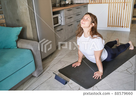 Young woman going yoga exercise at kitchen. Health care online lessons Young woman going yoga exercise at kitchen. Health care online lessons 88579660