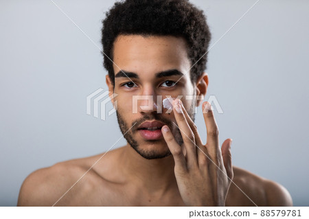 Young african american man applies moisturizer on his face. Male skin care. 88579781