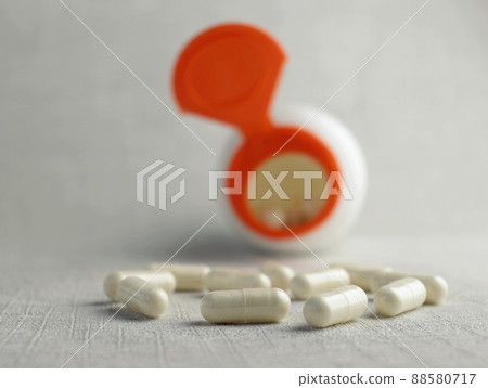 Glucosamine chondrotin capsules on the background of an open jar. Light gray textured background, close-up, selective focus. Glucosamine chondrotin capsules on the background of an open jar. Light gray textured background, close-up, selective focus. 88580717