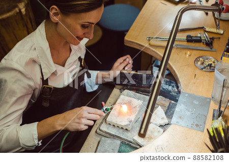 Goldsmith working on a hot glowing ring at her workbench Goldsmith working on a hot glowing ring at her workbench 88582108