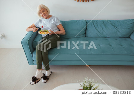 Aged woman eating on sofa at home Aged woman eating on sofa at home 88583818