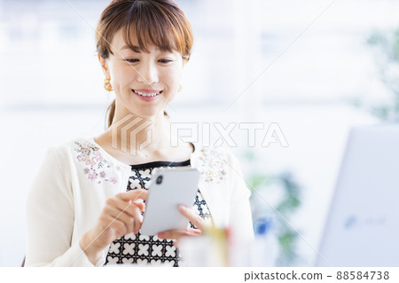 A woman who opens a laptop and operates a smartphone A woman who opens a laptop and operates a smartphone 88584738