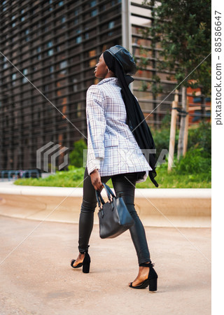 Back view full body of African American female in trendy outfit with Muslim headscarf walking with bag towards modern business building in city park Back view full body of African American female in trendy outfit with Muslim headscarf walking with bag towards modern business building in city park 88586647