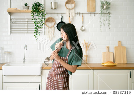Asian young woman dancing in kitchen room. She happy and relaxing at free time on weekend Asian young woman dancing in kitchen room. She happy and relaxing at free time on weekend 88587319