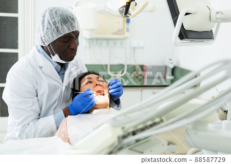 Professional dentist performing teeth treatment to woman at dental clinic 88587729