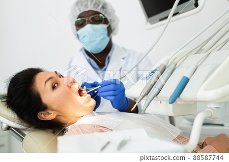 Dentinst examining oral cavity of woman in dental clinic 88587744