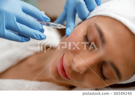 Closeup of young woman receiving hyaluronic acid injection in cheekbones at beauty salon Closeup of young woman receiving hyaluronic acid injection in cheekbones at beauty salon 88589240