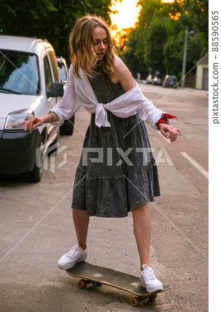 Millennial Woman in dress riding a skateboard on street. Skater girl on a longboard. Cool female skateboarder at sunset. Carefree female skater 20s enjoying freedom youth lifestyle Hobby Millennial Woman in dress riding a skateboard on street. Skater girl on a longboard. Cool female skateboarder at sunset. Carefree female skater 20s enjoying freedom youth lifestyle Hobby 88590565