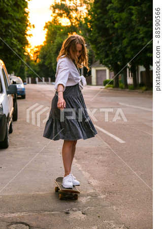 Millennial Woman in dress riding a skateboard on street. Skater girl on a longboard. Cool female skateboarder at sunset. Carefree female skater 20s enjoying freedom youth lifestyle Hobby Millennial Woman in dress riding a skateboard on street. Skater girl on a longboard. Cool female skateboarder at sunset. Carefree female skater 20s enjoying freedom youth lifestyle Hobby 88590566