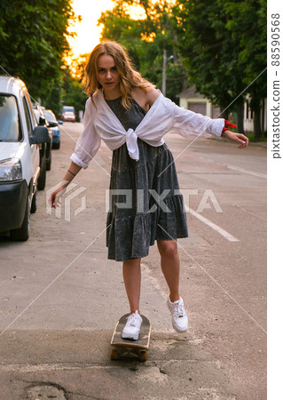 Millennial Woman in dress riding a skateboard on street. Skater girl on a longboard. Cool female skateboarder at sunset. Carefree female skater 20s enjoying freedom youth lifestyle Hobby Millennial Woman in dress riding a skateboard on street. Skater girl on a longboard. Cool female skateboarder at sunset. Carefree female skater 20s enjoying freedom youth lifestyle Hobby 88590568