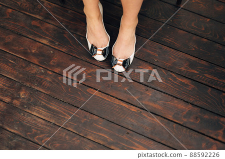 Female legs in graceful white ballet shoes with black bows on a wooden floor, close-up  88592226