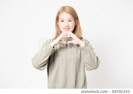 Young woman standing in front of a white background and making a heart shape with her hands Young woman standing in front of a white background and making a heart shape with her hands 88592243