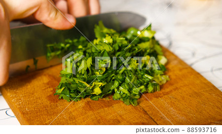 A close-up of a woman's hand with a knife is chopping parsley on a cutting board. Healthy and wholesome food. A close-up of a woman's hand with a knife is chopping parsley on a cutting board. Healthy and wholesome food. 88593716