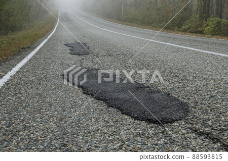 Fresh patches after patching the road. Country highway in the foggy forest. Bad road condition. 88593815