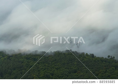 The view from the top of the green forest is obscured by mist. Through the fog you can see the poles of the power lines. It's a beautiful landscape. The view from the top of the green forest is obscured by mist. Through the fog you can see the poles of the power lines. It's a beautiful landscape. 88593885