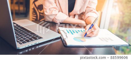 Woman analyzing data graph the stock situation.She uses a pen and a laptop computer. Woman analyzing data graph the stock situation.She uses a pen and a laptop computer. 88599606