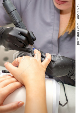 Manicure master in rubber gloves applies an electric nail file to remove the nail polish in a nail salon Manicure master in rubber gloves applies an electric nail file to remove the nail polish in a nail salon 88599739