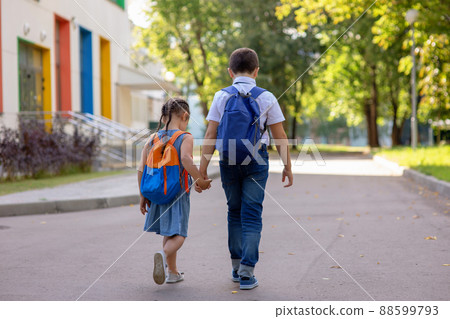 Cheerful schoolchildren, a little girl and a boy in a white shirt with backpacks go on the way to school. 88599793