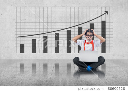 Asian nerd with ugly face sitting while using a laptop with shocked expression with decreased graph Asian nerd with ugly face sitting while using a laptop with shocked expression with decreased graph 88600328