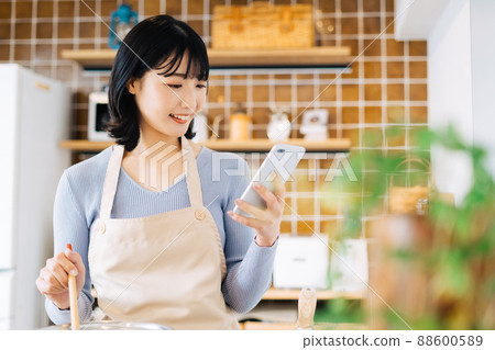 A woman cooking while watching a smartphone 88600589