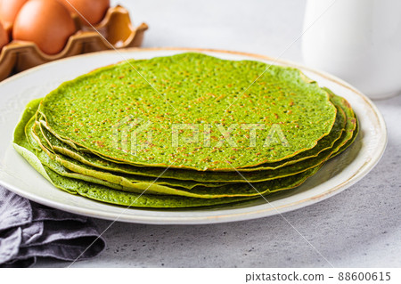 Stack of spinach crepes on plate. Green vegan pancakes, gray background. Healthy breakfast recipe. Stack of spinach crepes on plate. Green vegan pancakes, gray background. Healthy breakfast recipe. 88600615
