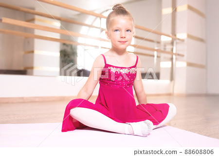 Baby girl wearing a peach tutu. a smiling baby girl is Sitting and stretching out on a sports mat. 88608806
