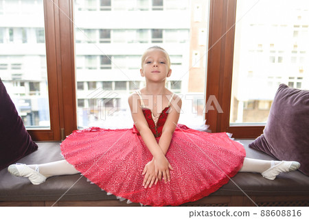 Smiling baby girl dreaming to become professional ballet dancer, classical dance school. the little girl ballerina does stretching sitting against the window 88608816