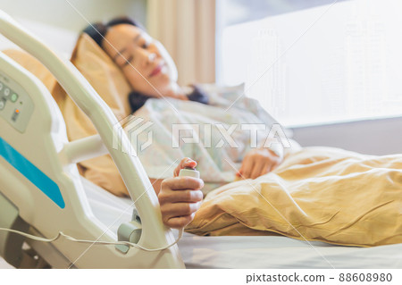 Woman patient holding emergency call button while lying in hospital bed. Woman patient holding emergency call button while lying in hospital bed. 88608980