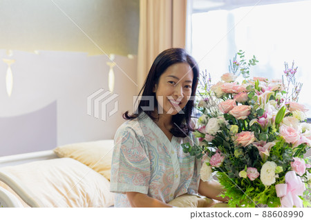 Woman patient smiling and holding a flower bouquet sitting on hospital bed. 88608990