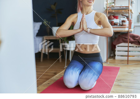 Sportive lady in top and leggings holds hands in namaste mudra sitting on mat Sportive lady in top and leggings holds hands in namaste mudra sitting on mat 88610793