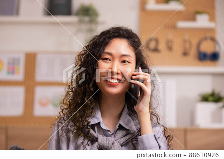 Phone conversation. Confident Asian woman sit on couch talk speak communicate by telephone from home holding device at ear. 88610926