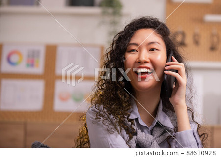 Phone conversation. Confident Asian woman sit on couch talk speak communicate by telephone from home holding device at ear. Phone conversation. Confident Asian woman sit on couch talk speak communicate by telephone from home holding device at ear. 88610928