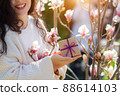 Woman holding gift box on flowers background. Female hands holding beautiful present with violet bow. Festive background. 88614103