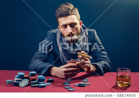 A wealthy mature man drinking brandy and playing poker with the excitement in a casino.  88614930