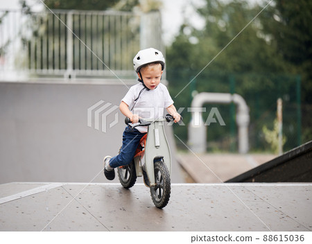 Child riding balance bike. Male toddler kid in helmet learning to ride on run bicycle at skate park. Child riding balance bike. Male toddler kid in helmet learning to ride on run bicycle at skate park. 88615036
