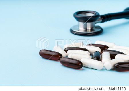 Assorted brown and white capsules, stethoscope, pills, isolated on blue background. Nutritional supplements for weight loss and energy, dietary aids. Health care concept. Copy space Assorted brown and white capsules, stethoscope, pills, isolated on blue background. Nutritional supplements for weight loss and energy, dietary aids. Health care concept. Copy space 88615123