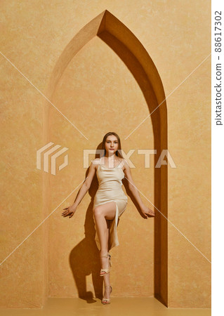 Cute young woman in silky spaghetti strap dress standing in middle eastern style arch Cute young woman in silky spaghetti strap dress standing in middle eastern style arch 88617302