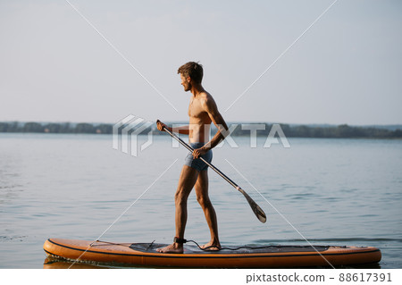 young men with a paddle standing on a sapboard. 88617391