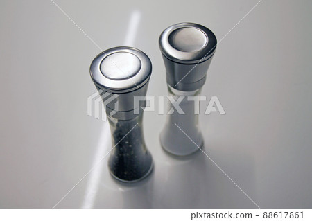 Salt and pepper glass and iron grinders on a white desk Salt and pepper glass and iron grinders on a white desk 88617861