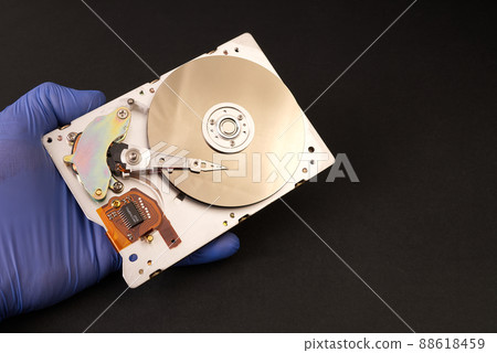 Hard drive in the hands of the master. male hands in blue gloves hold hdd. Computer industry. Disassembled hard drive from the computer 3.5' SATA on dark, black background 88618459