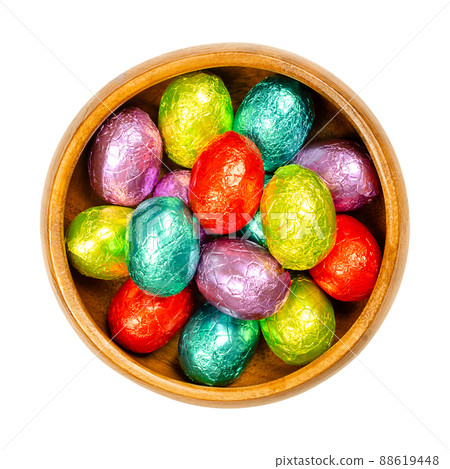 Mixed colored foil wrapped chocolate Easter Eggs, in a wooden bowl. Mini chocolate eggs, sweet candy, wrapped in aluminum foil of different colors. Isolated from above, over white, macro food photo. 88619448