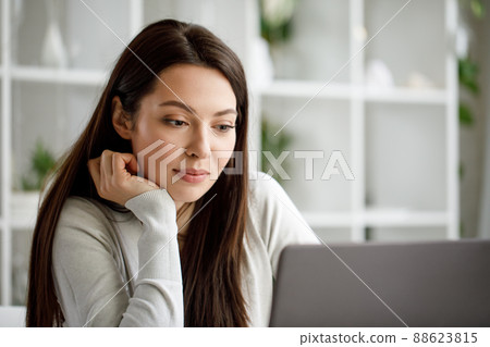 Portrait of a brunette woman working in an office with a laptop computer. A woman with a laptop looks into the camera and smiles sweetly. 88623815