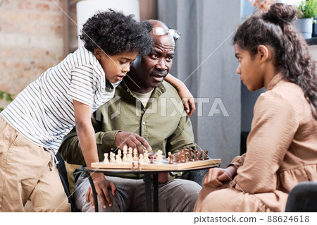 Senior African American man and his two grandchildren playing chess together 88624618