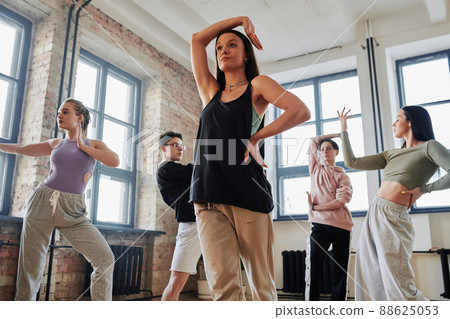 Contemporary female performer in activewear keeping right arm over her head 88625053