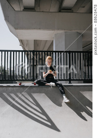 A European female skater with red hair is riding a skateboard on a skate pad. a woman in black clothes and a skateboard or a longboard is engaged in active sports 88628478