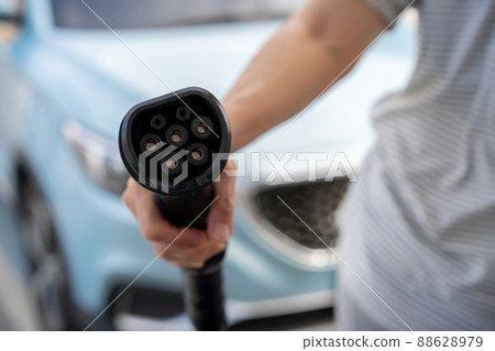 Unrecognizable Asian woman holding AC type 1 EV charging connector at EV charging station, woman preparing an EV - electric vehicle charging connector for recharge a vehicle. Unrecognizable Asian woman holding AC type 1 EV charging connector at EV charging station, woman preparing an EV - electric vehicle charging connector for recharge a vehicle. 88628979