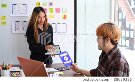 Beautiful creative woman holding digital tablet and presenting mobile app interface design to her colleagues. 88629356