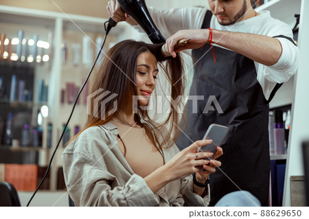 Beautiful woman with long hair using smart phone at beauty salon Beautiful woman with long hair using smart phone at beauty salon 88629650