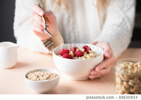 Young woman eating oatmeal porridge with raspberries Young woman eating oatmeal porridge with raspberries 88630933